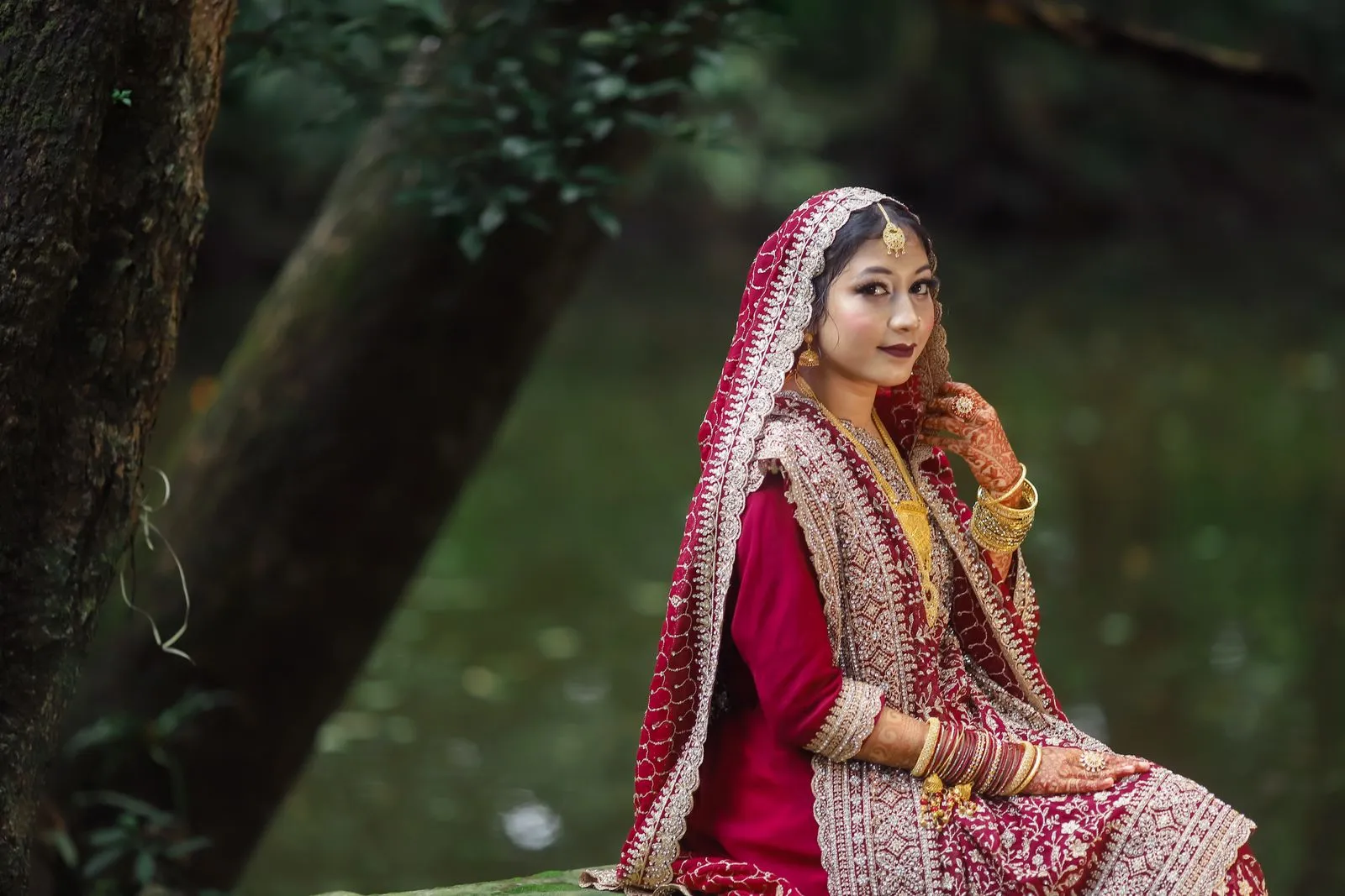 Stunning bride in vibrant traditional attire poses gracefully by a serene lake.